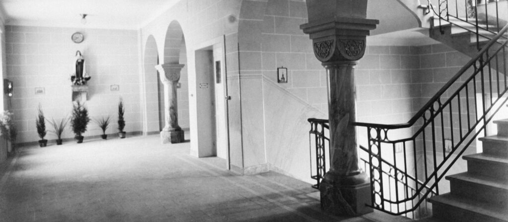 Photo d’une unité de soins de la clinique Ste Zithe. La clinique Ste Zithe était dirigée par des religieuses et leur appartenait aussi (Religieuses Tertiaires du Mont Carmel). Tous les jours, on célébrait une messe dans la chapelle de la clinique. Des tableaux, des statues et de la décoration en relation avec la religion catholique se trouvaient dans chaque chambre. L’architecture visible sur cette photo existe encore aujourd’hui, bien que les lieux aient changé au cours des dernières 60 années 5 à 6 fois (soins intensifs, dialyse, rééducation, salles d’examen, clinique du jour). L’ameublement et l’architecture se sont adaptés aux nouvelles méthodes de traitement et de diagnostique.