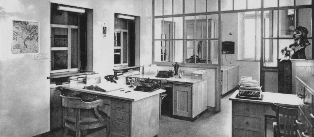 Photo de la comptabilité avec la centrale téléphonique. C’étaient surtout des dames, sous la responsabilité d’une religieuse, qui y ont travaillé. La plupart du temps, les factures étaient réglées en liquide ou par chèque. La plus grande partie de documents était inscrite manuellement dans des grands livres de caisse ou de comptabilité. De même, les salaires du personnel étaient payés en liquide. Plus tard, on les a réglés par virement bancaire. A cette époque, on avait aussi plusieurs caisses de maladie, là où aujourd’hui on n’a qu’une Caisse de Santé commune. On ne disposait ni d’ordinateurs, ni de machine à copier. Les copies étaient réalisées à l'aide d'une machine à écrire et de papier calque. La centrale téléphonique avait un numéro à cinq chiffres. On devait faire une demande à la Poste pour faire un appel à l’étranger.